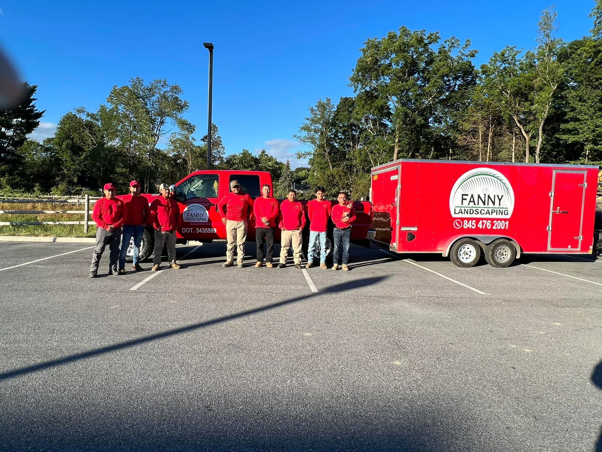 Group of people in red shirts standing next to a red truck and trailer with