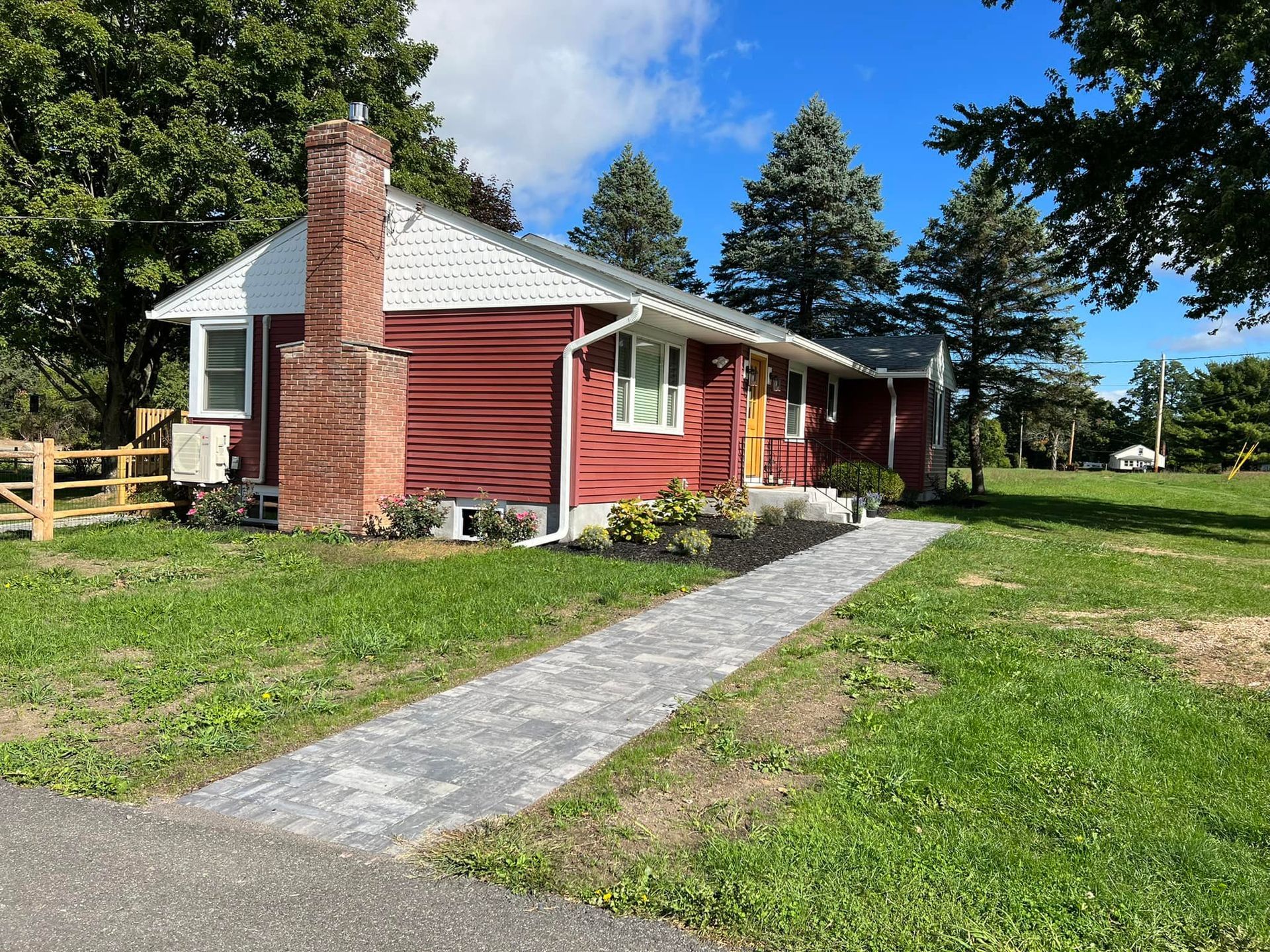 Red house with stone pathway, brick chimney, green lawn, blue sky.
