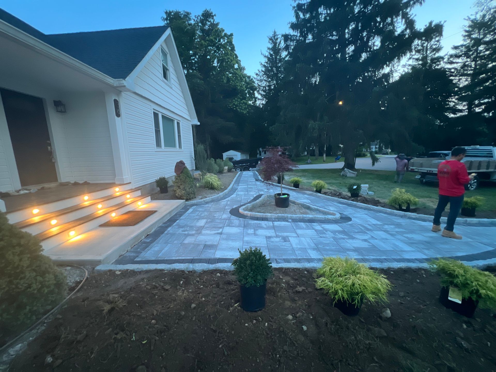 Brick walkway leads to white house, with landscaping and person in red jacket.
