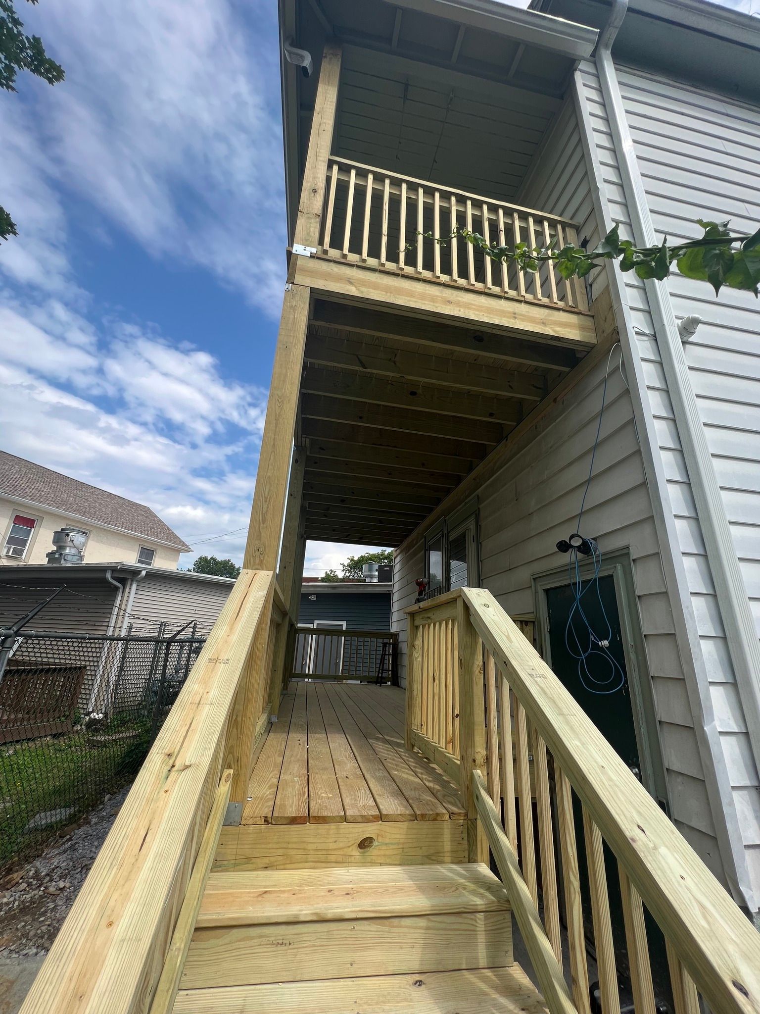 Wooden staircase leading to a second-story deck with a blue sky in the background.