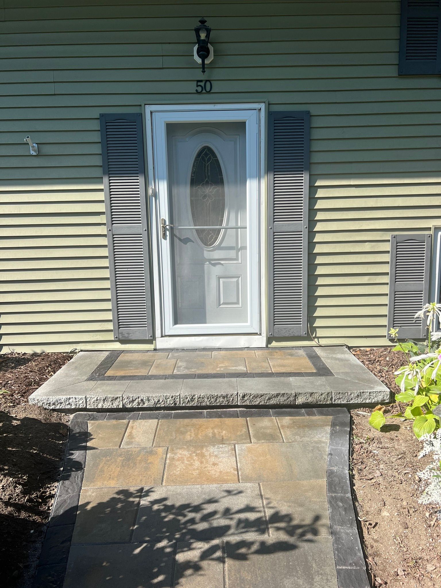 Front door with porch and steps, green siding, shutters, and a doormat.