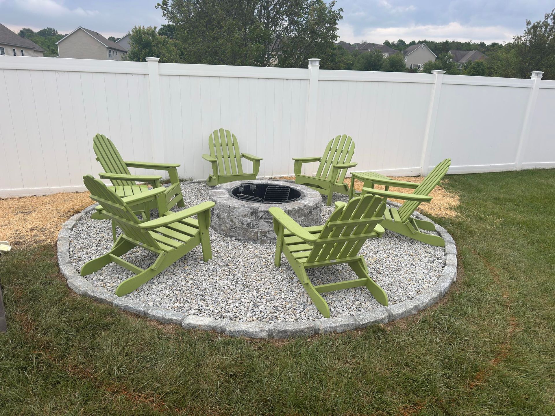 Fire pit with lime green Adirondack chairs in a fenced yard.