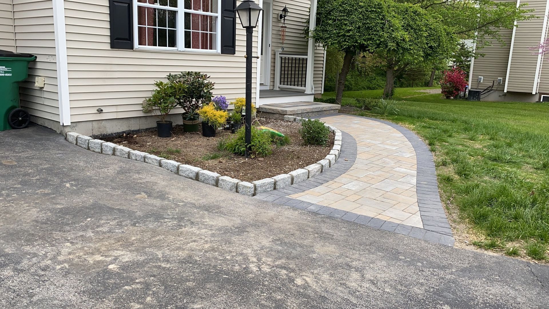 A paved walkway curves from a driveway to a house entrance with a small garden.