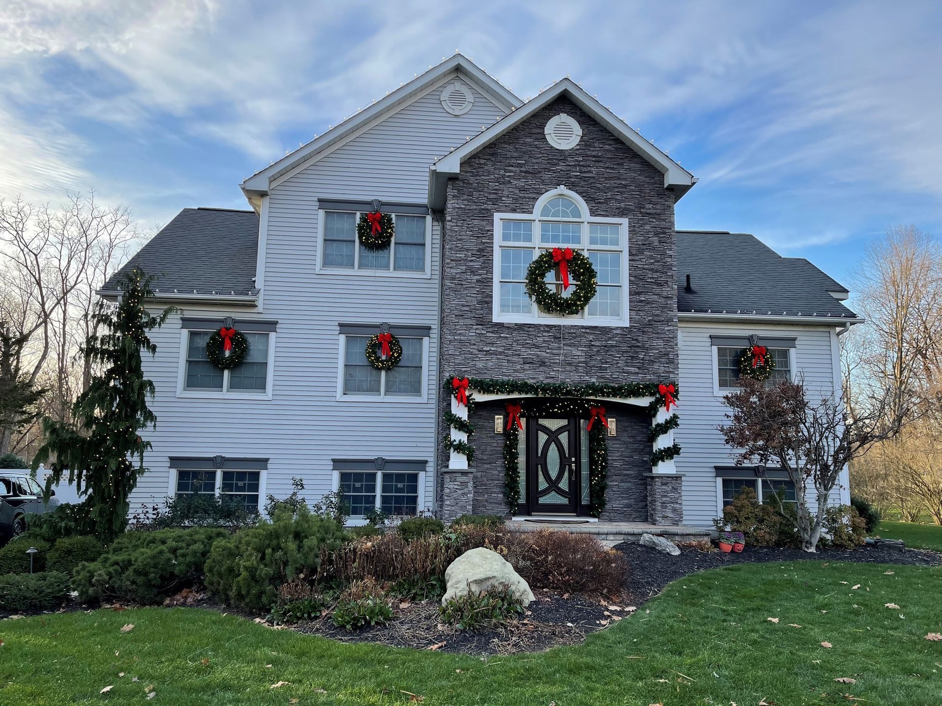 Two-story house decorated with Christmas wreaths and garlands, with a blue sky background.