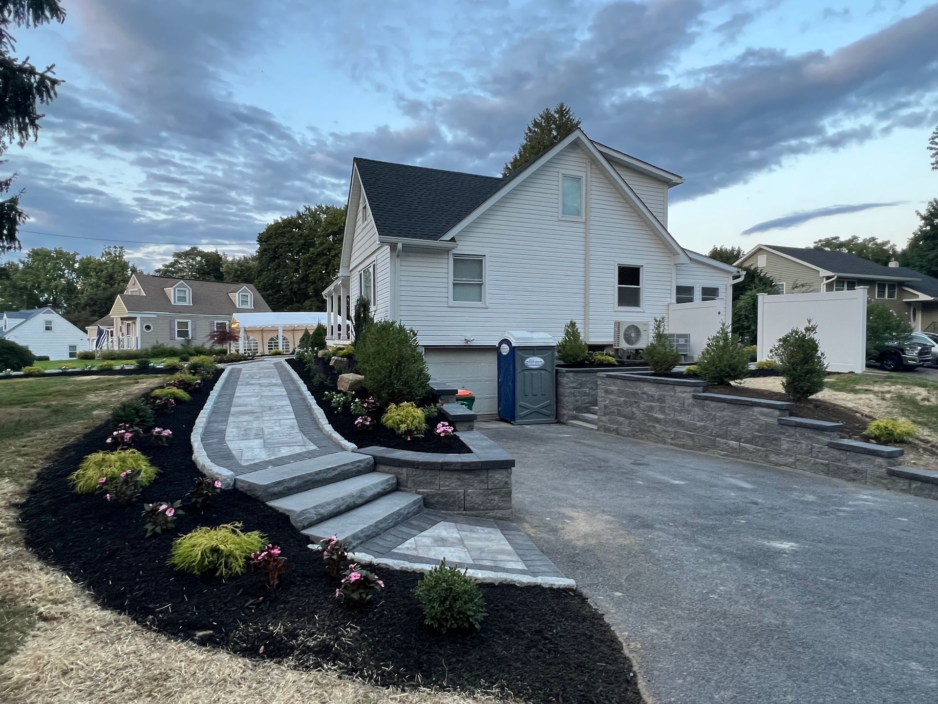 Stone walkway and steps lead up to a white house, with a dark mulch flower bed on the left.
