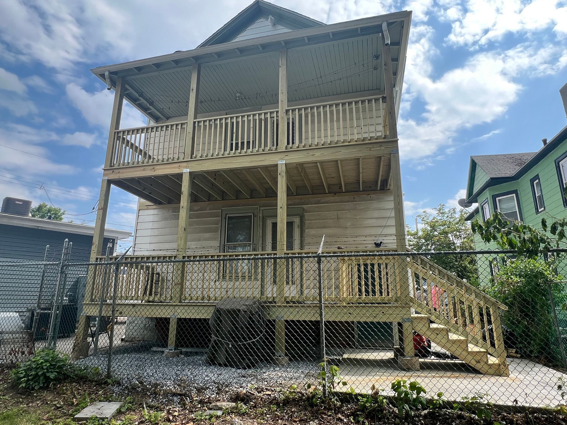 Back of two-story white house with wooden decks.  A fence and stairs lead down to a yard.