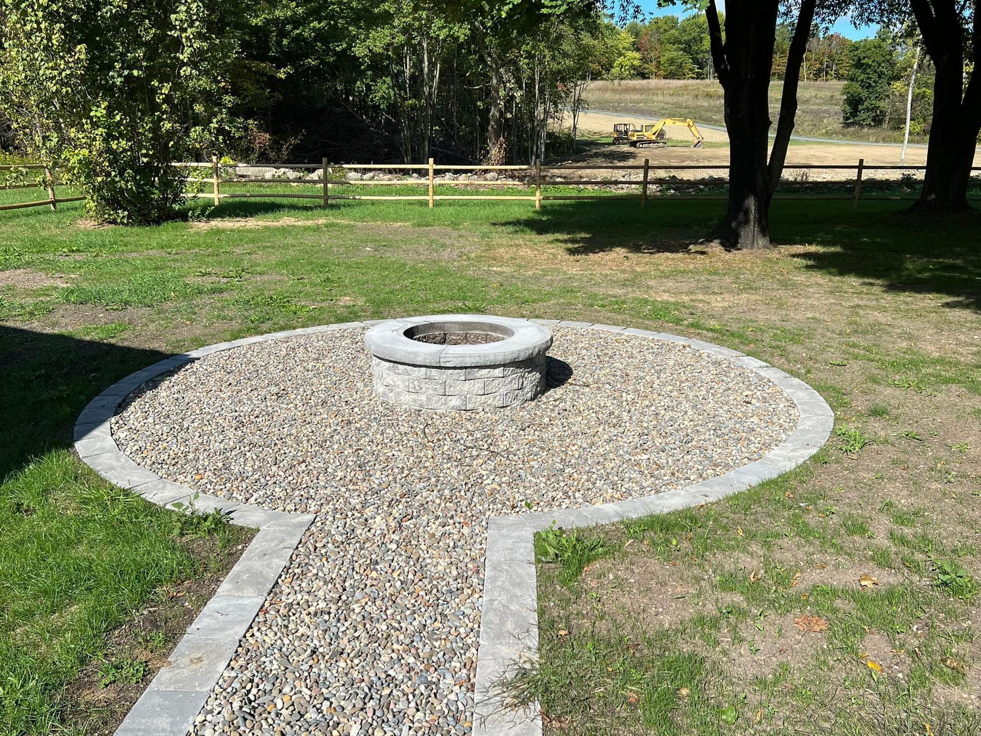 A stone fire pit in a gravel circle with a stone walkway in a grassy yard.