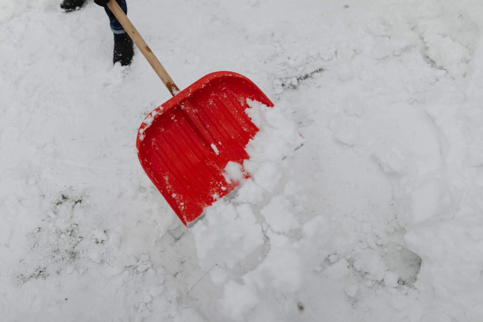 Red snow shovel scooping up snow outdoors.
