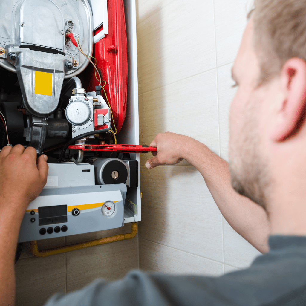 Man working on a boiler, using a wrench. The boiler is mounted on a tiled wall.