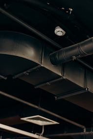 Black ventilation ducts and pipes against a dark ceiling, with a security camera visible.