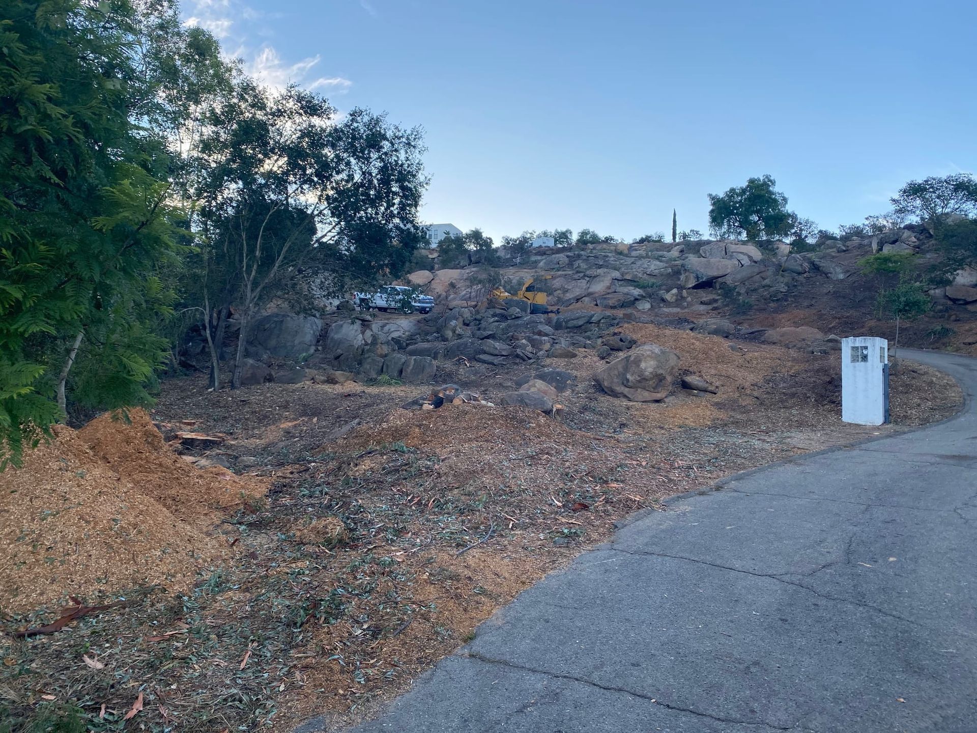 A barren hillside with a paved road in the foreground and a white mailbox. The sky is blue.