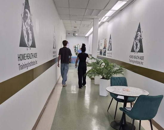 White hallway with wall graphics, potted plants, and two people walking away.