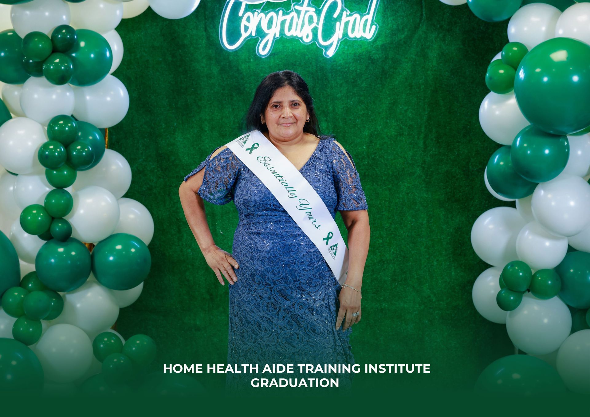 A woman in a blue dress is standing in front of a green and white balloon arch.