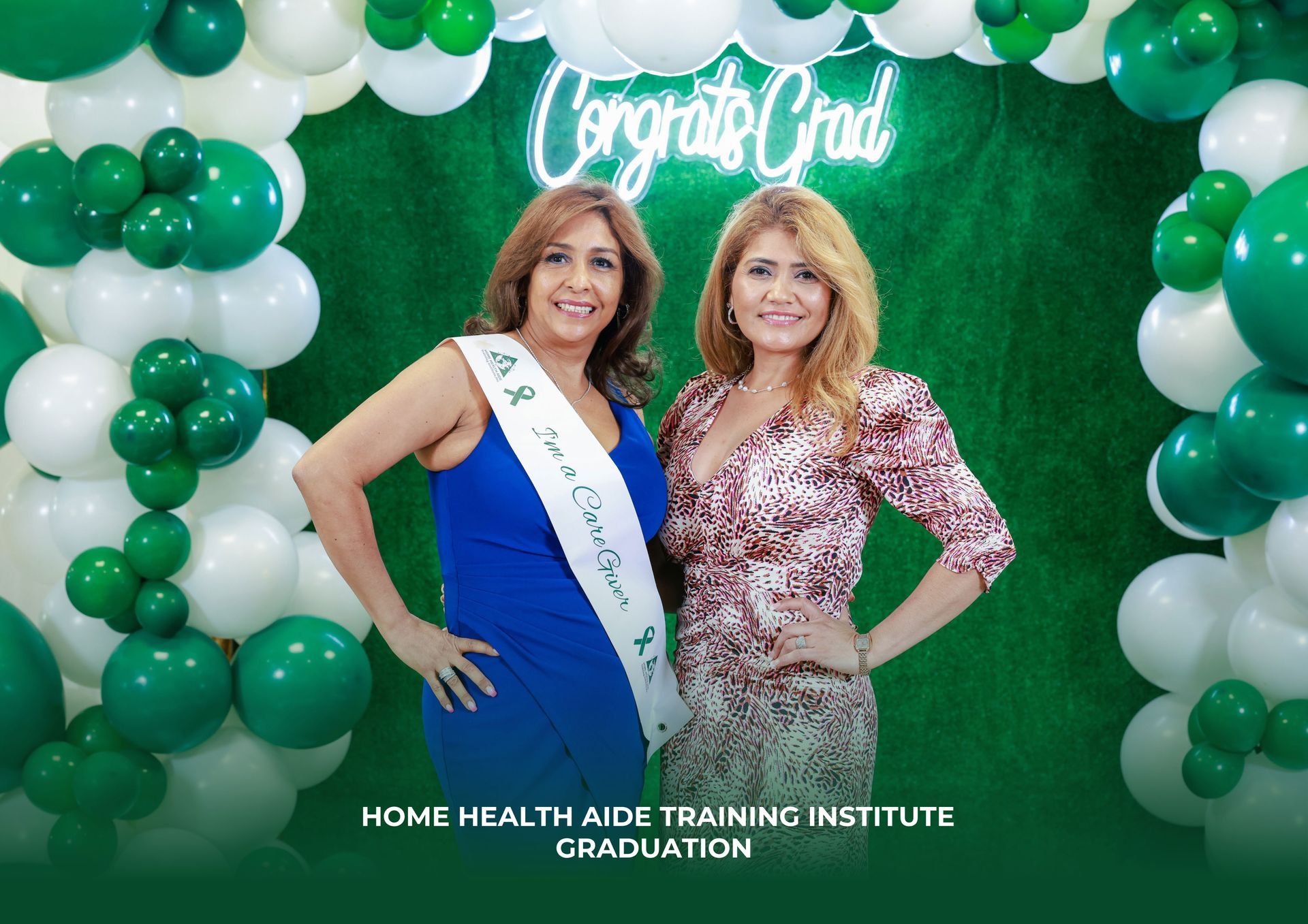 Two women are posing for a picture in front of a wall of green and white balloons.