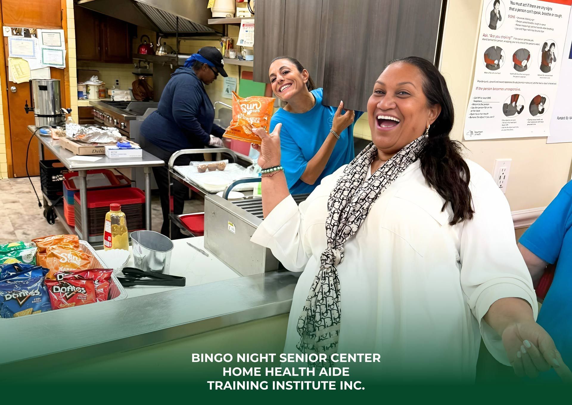 People in a kitchen smiling, one giving a thumbs up. Snacks and supplies are on a counter.