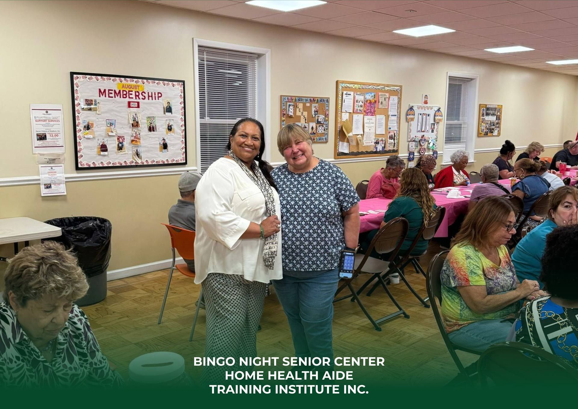 Two women smiling at a senior center event. People seated at tables, room with decorations.