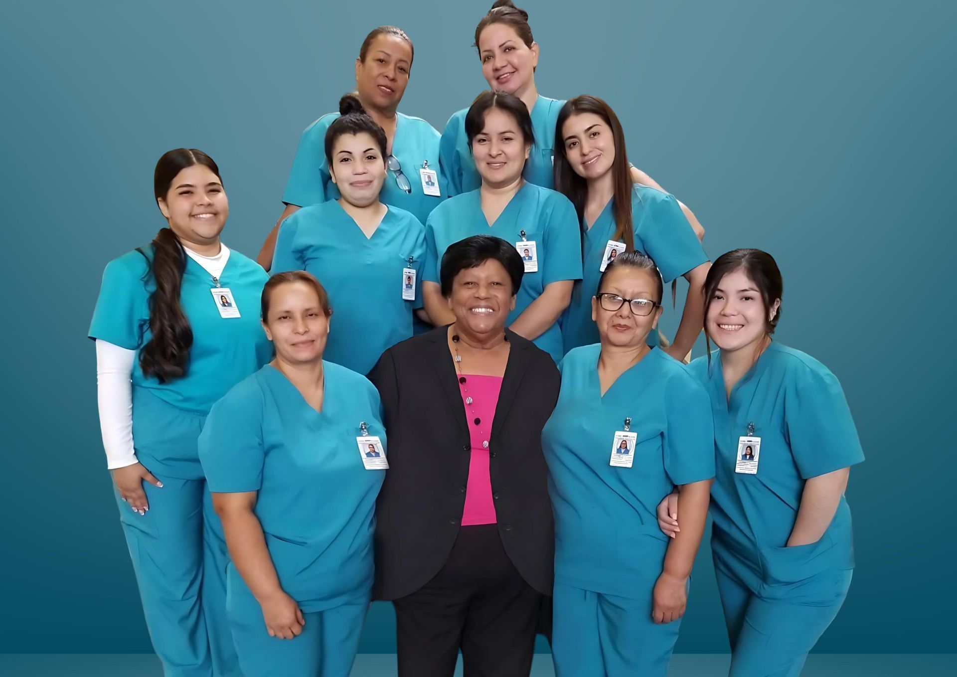 A group of women in scrubs is standing around a table with food and a cake.