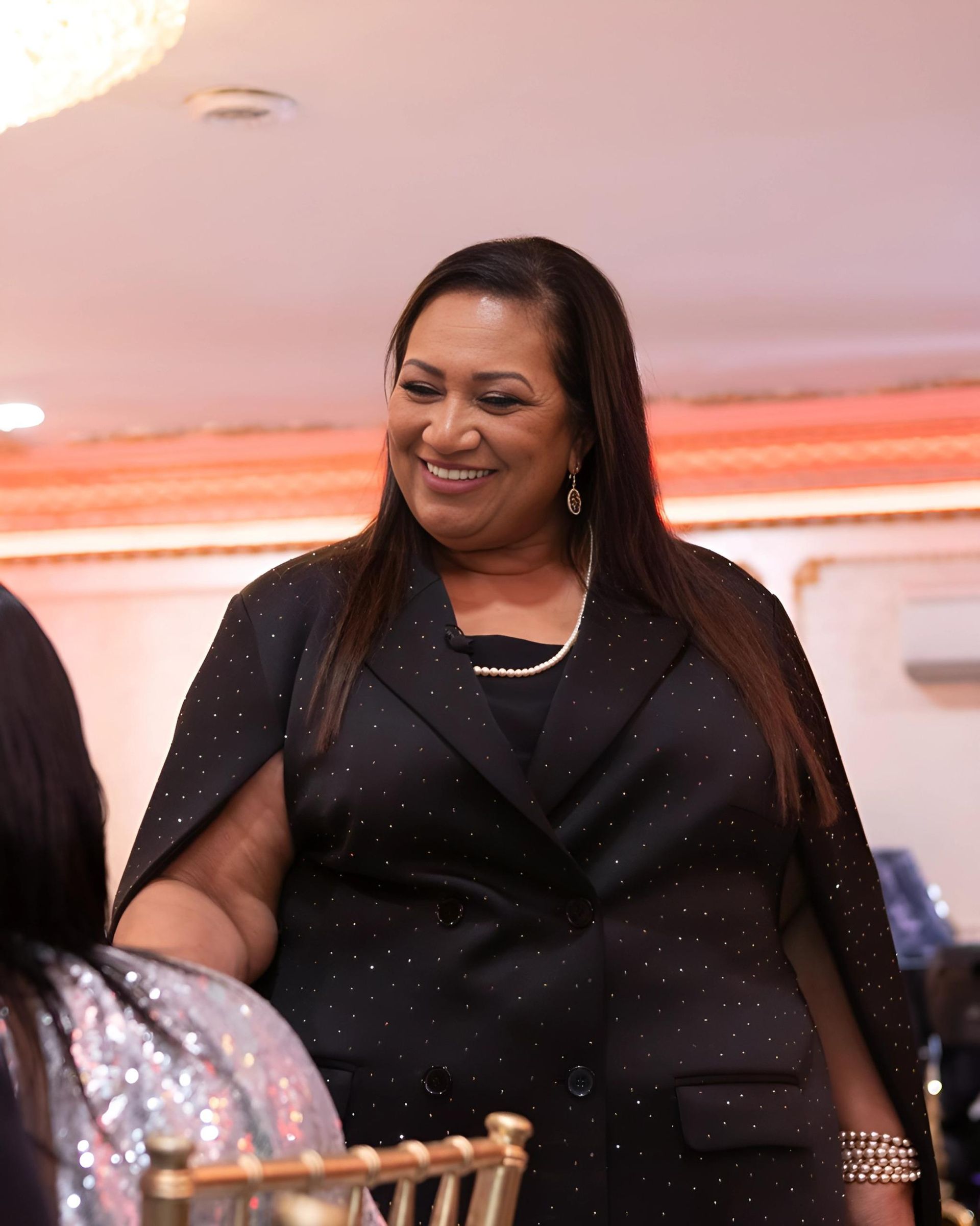 A woman in a black dress and cape is smiling.