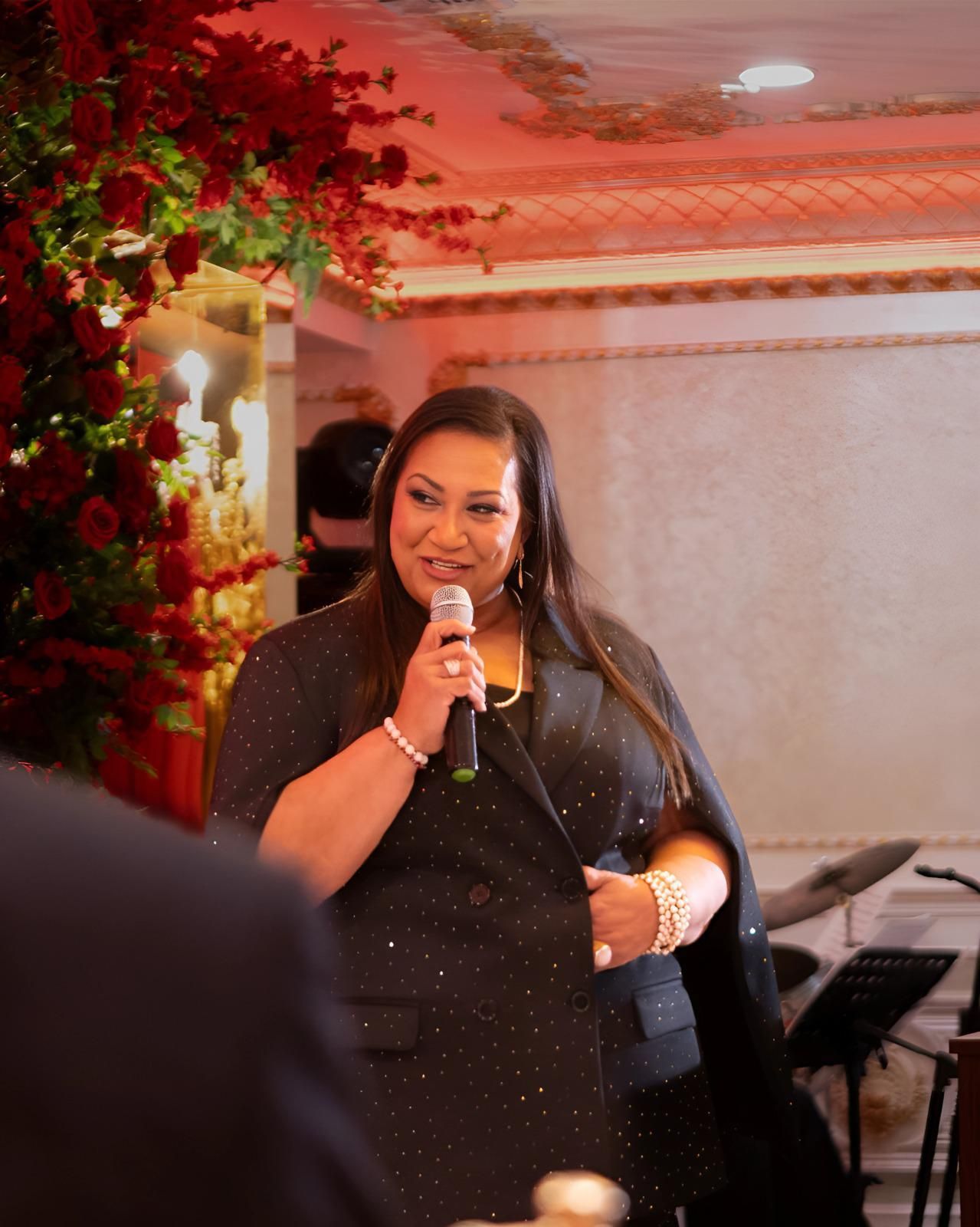 A woman in a black dress is holding a microphone and smiling.
