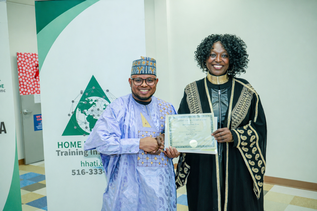 A man and a woman pose together holding a certificate in front of a branded Home Health Aide Training sign.