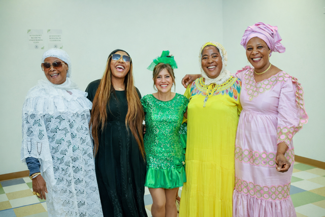 Five people stand side-by-side in a room, smiling and posing for a group photo in diverse, colorful formal attire.