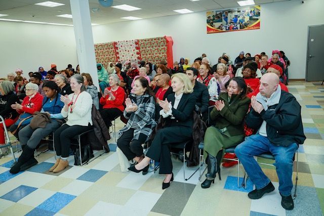 A diverse group of people sitting in a brightly lit room, clapping during an indoor event.
