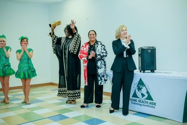 Five people stand in a room, some clapping or cheering behind a table labeled 