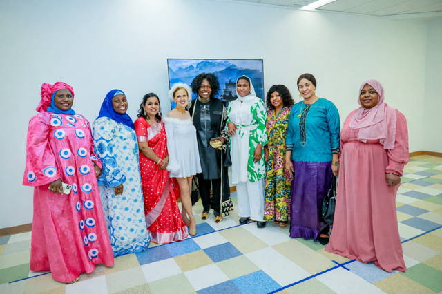 A group of ten diverse individuals stand in a line against a plain wall, posing for a photo in varied traditional attire.