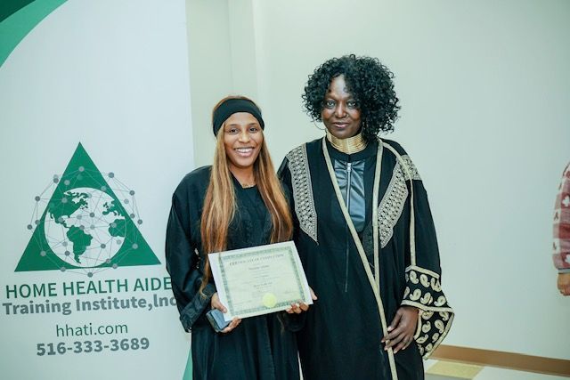 A person holds a certificate standing next to an instructor in front of a Home Health Aide Training Institute banner.