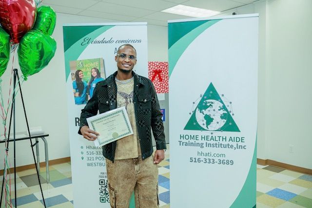 A person smiling while holding a certificate in front of Home Health Aide Training Institute banners and balloons.