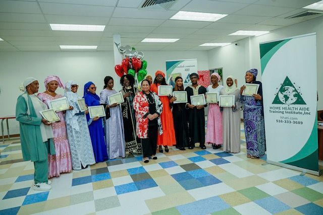A group of people standing in a row in a bright hall, holding certificate folders next to a branded event banner.