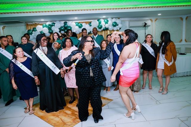 A group of people wearing event sashes at a party, with a person in a black suit holding a microphone and singing.