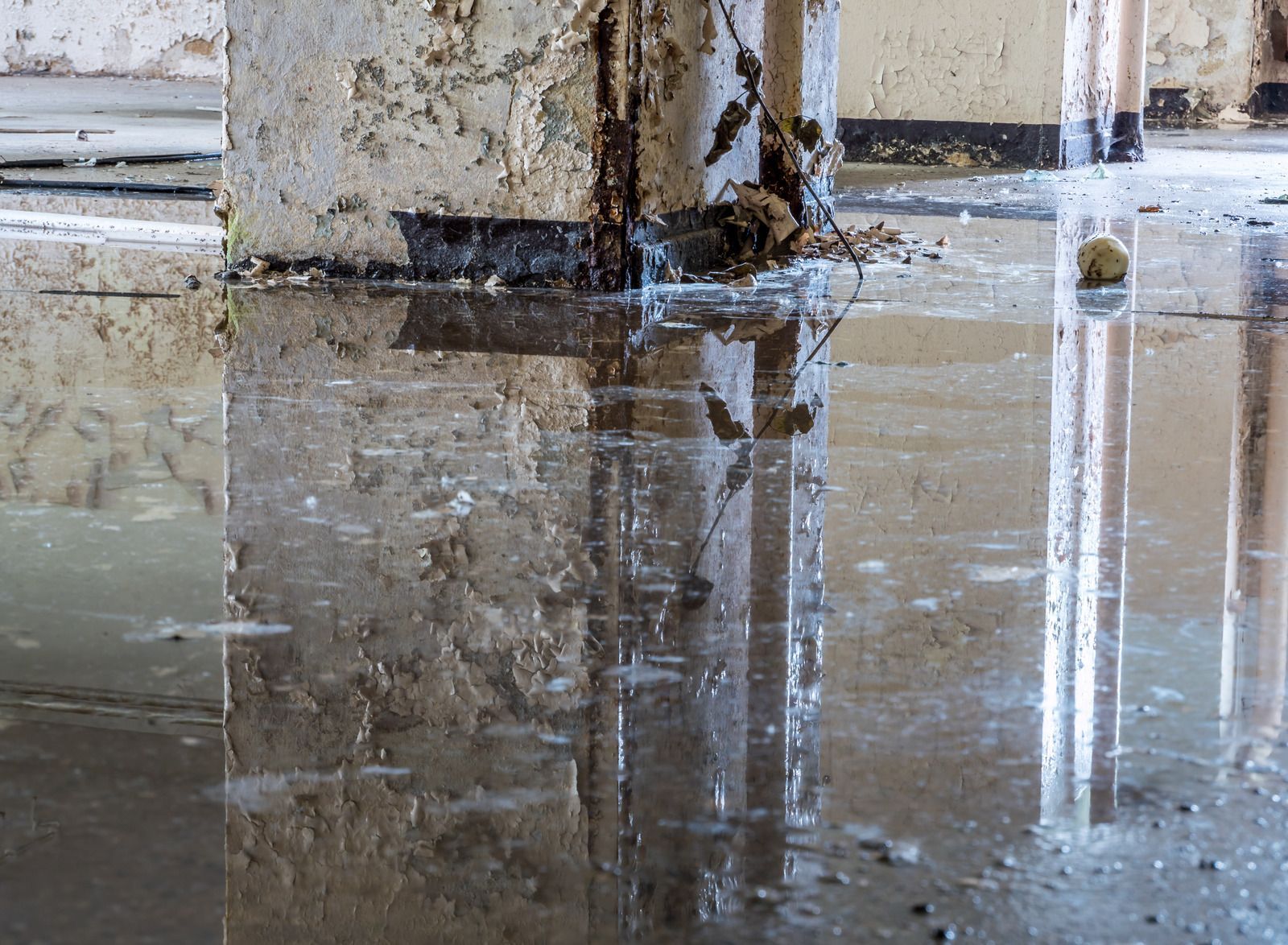 Water-covered floor reflects a concrete pillar in a derelict interior.