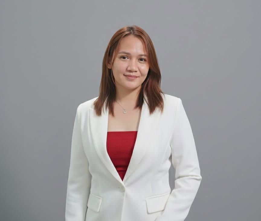 A person with shoulder-length hair wearing a white blazer over a red top against a solid gray background.
