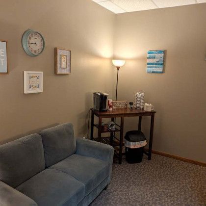 A waiting room with a sofa, a small table with coffee maker, and wall decorations.