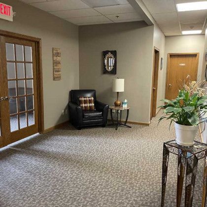 Hallway with seating area, brown doors, carpet, and a decorative plant.