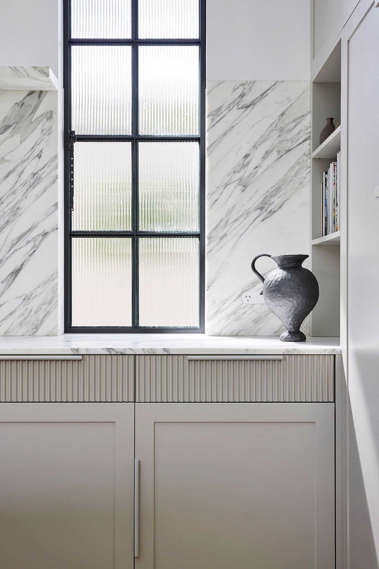 A vase is sitting on a counter next to a window in a kitchen.