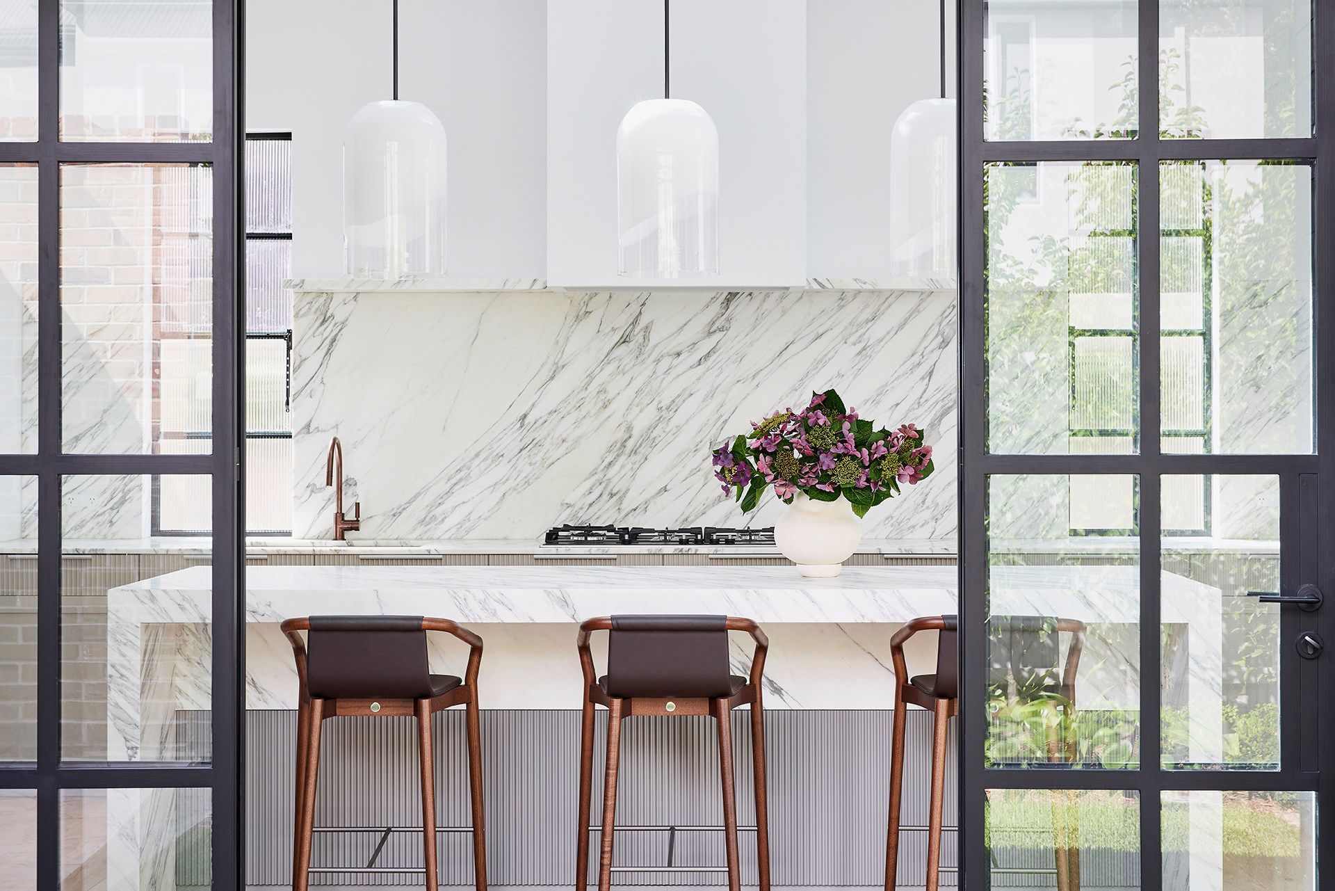 A kitchen with a marble counter top , stools , and a stove.