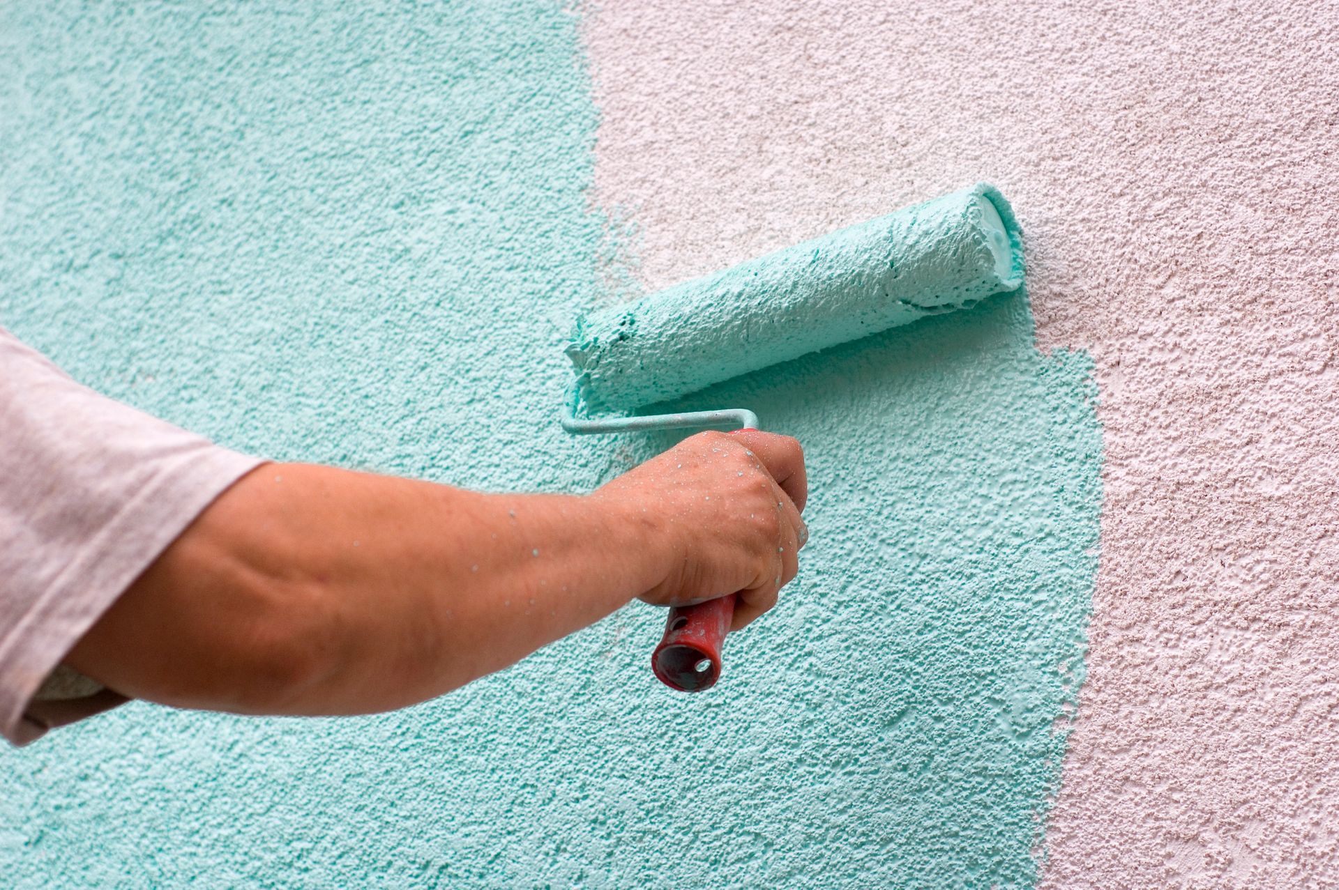 A person is painting a wall with a paint roller.