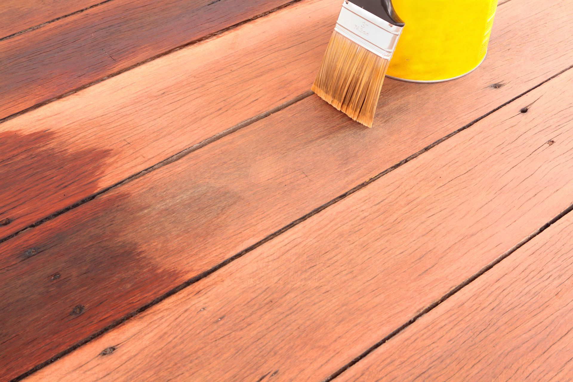 A brush is sitting on a wooden deck next to a yellow bucket.