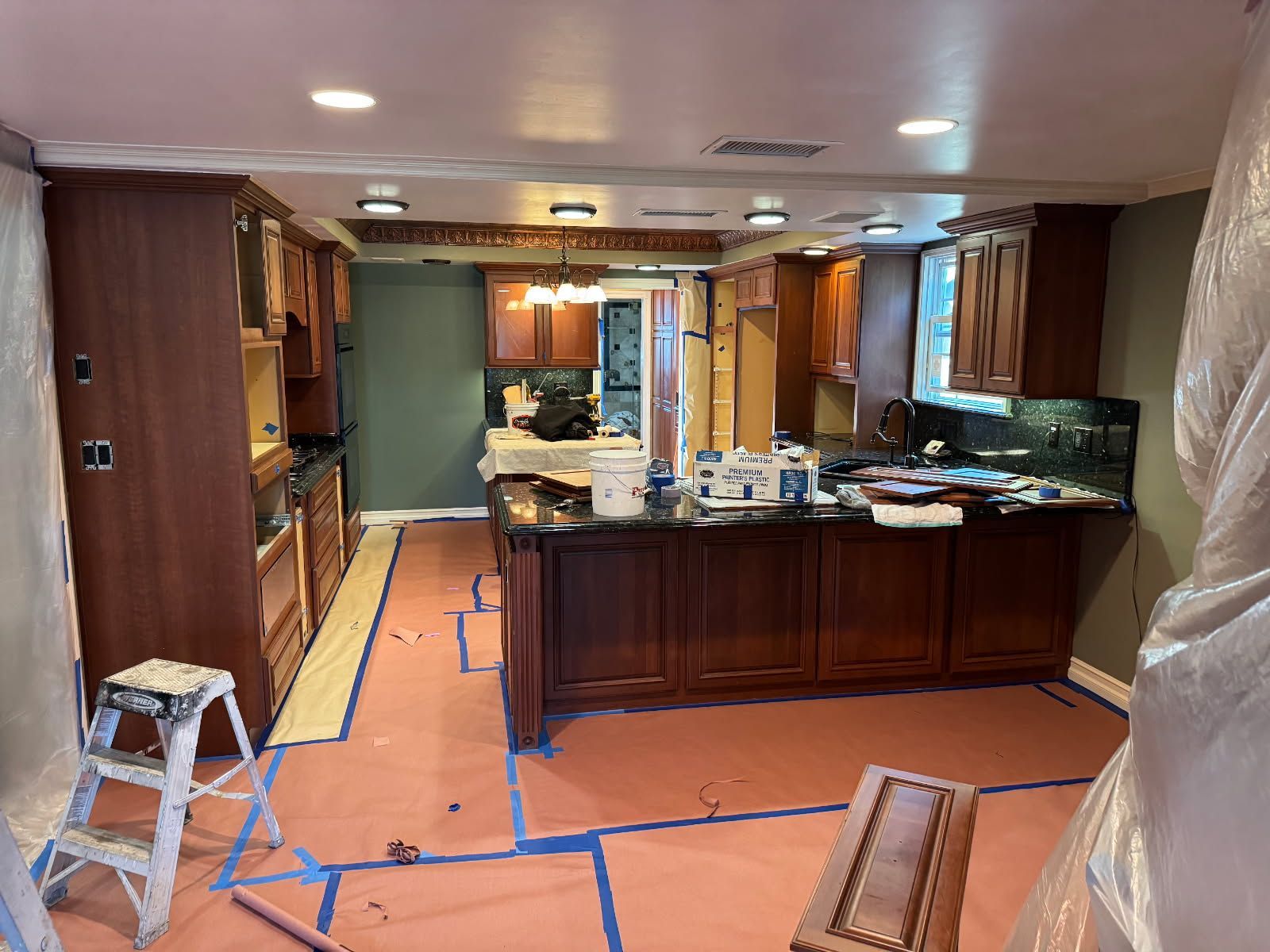 A kitchen is being painted and covered in plastic.