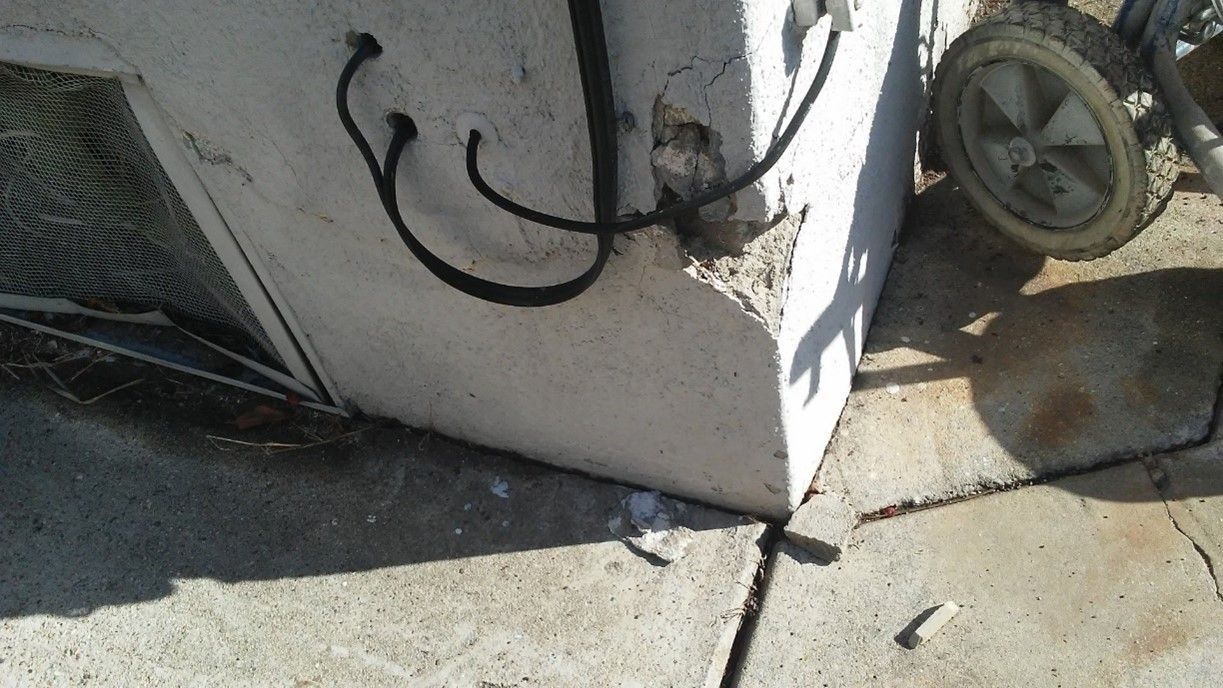 A concrete wall with a hook on it and a wheelbarrow in the background.