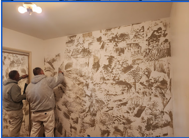A person is removing wallpaper from a wall with a spatula.