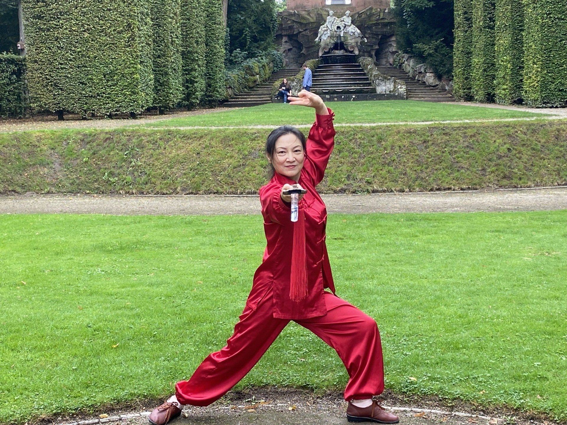 Eine Frau in einem roten Outfit übt in einem Park Kampfsport.