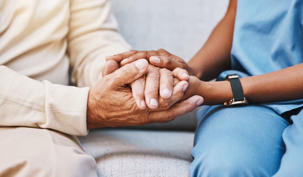 Hands clasped: An elderly person's hands are held by a person in blue scrubs, offering support and comfort.