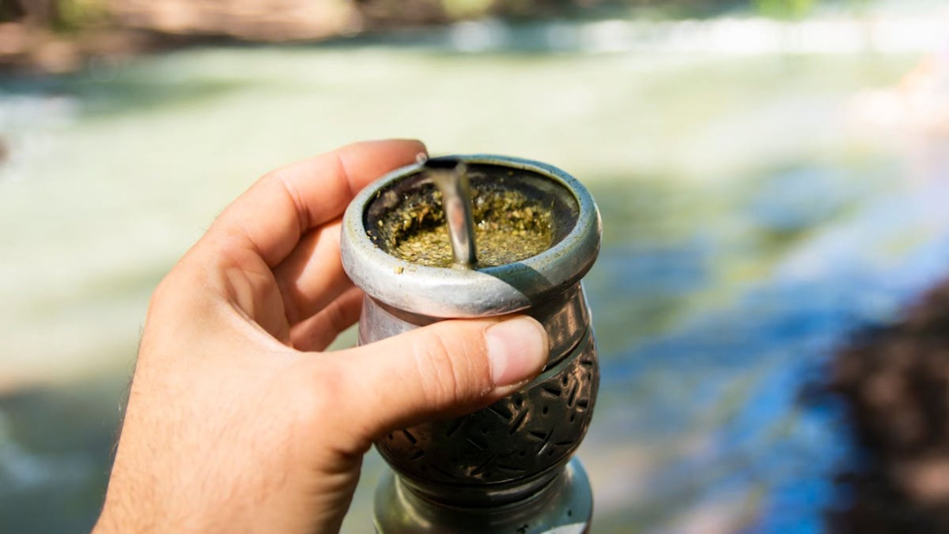 Mano sosteniendo un mate de plata lleno de yerba mate, agua borrosa en el fondo.
