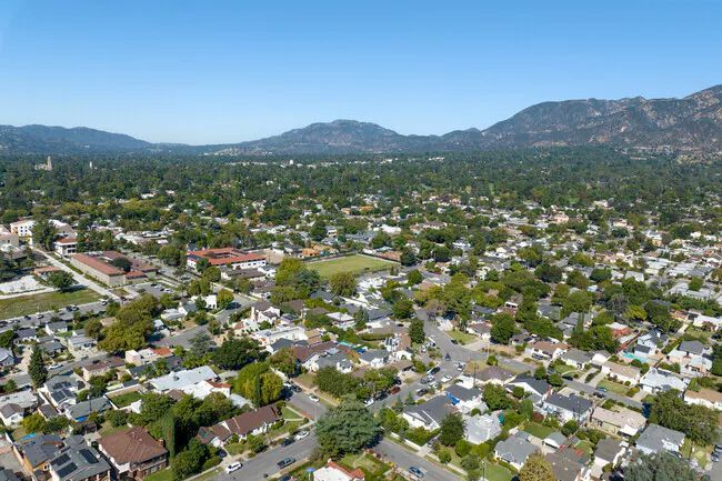 An aerial view of Altadena, CA with lush trees and houses, framed by distant rolling mountains.