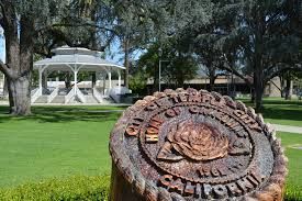 A wooden carving of the City of Temple City seal in the foreground, with a white gazebo in a park in the background.