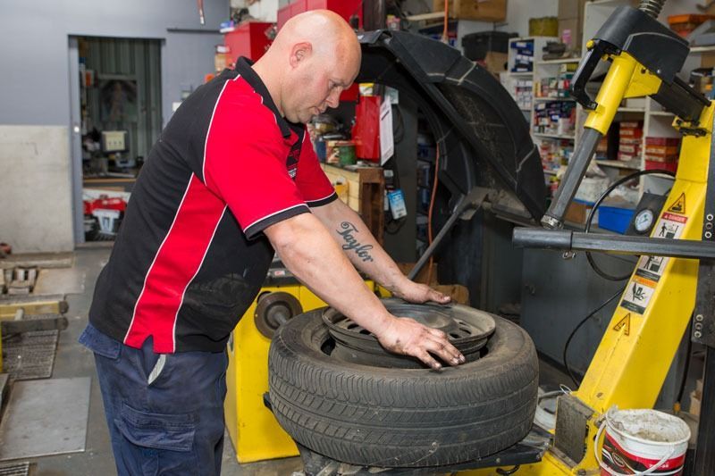 A Man Is Changing A Tire On A Machine In A Garage — CS Mechanical Repairs & Services In Wauchope, NSW