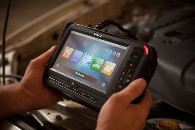 A Person Is Holding A Tablet In Their Hands In Front Of A Car Engine — CS Mechanical Repairs & Services In Wauchope, NSW